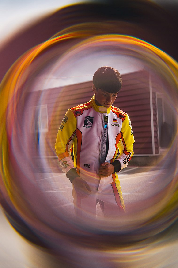 FIA Karting Academy Trophy Senior, Valencia 2026 – Constantin Papst Constantin Papst in Rennanzug, durch ein Objekt mit kreisförmiger Spiegelung fotografiert.