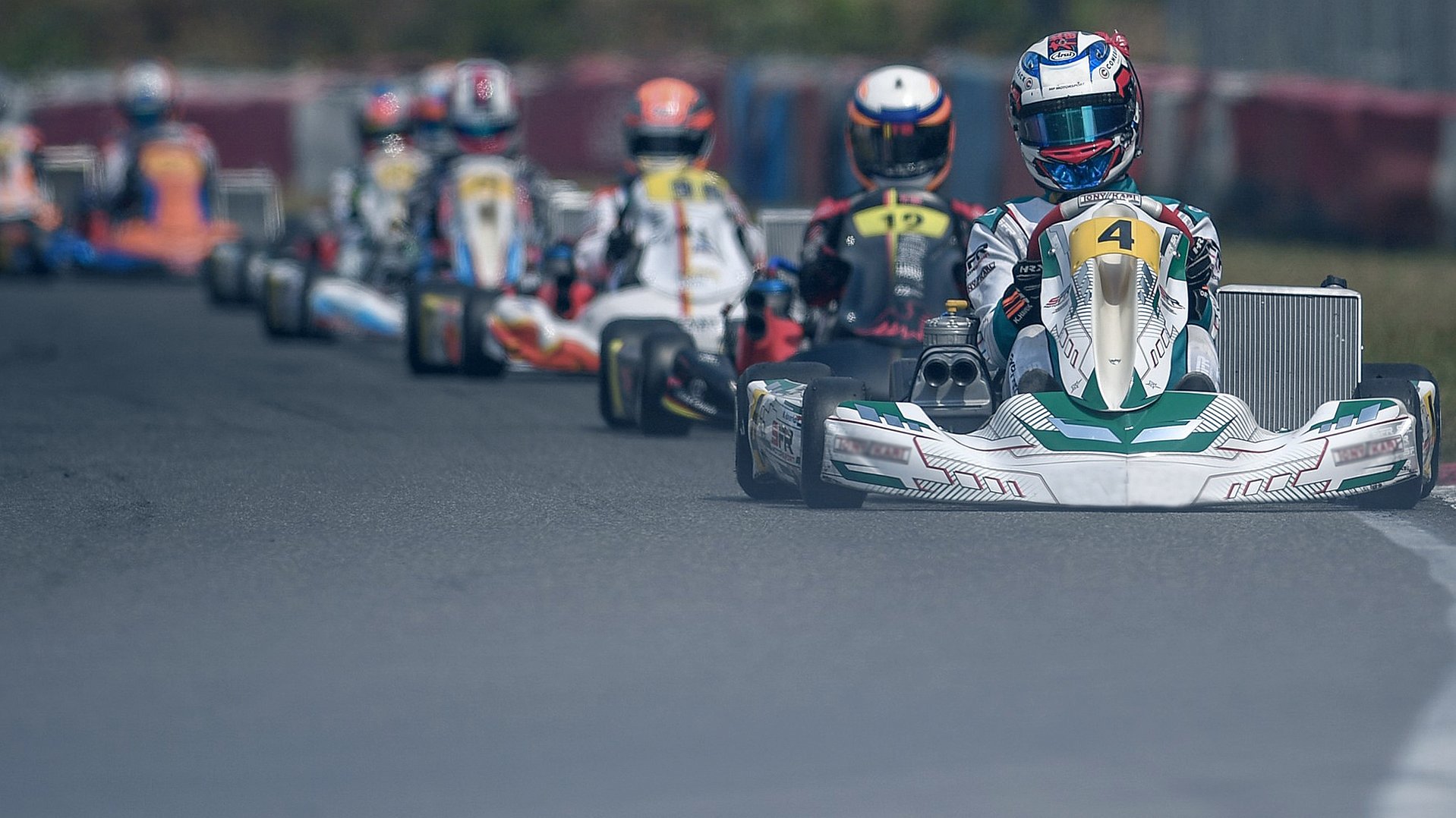 Go-Kart-Fahrer rasen um eine Strecke, wobei der Fahrer des Karts mit der Nummer 4 das Feld anführt.