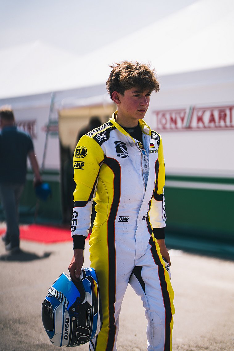 Stavros Tsotsos Francia steht in Rennanzug und mit Helm in der Hand vor dem Fahrerlager der FIA Karting Academy Trophy.