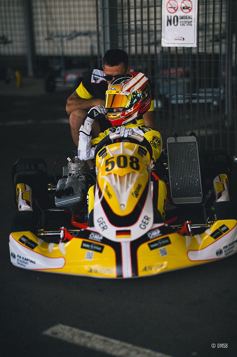 Stavros Tsotsos Francia, FIA Karting Academy Junior-Trophy 2026, Circuito Internazionale Napoli Stavros Tsotsos Francia sitzt mit Helm im gelb-weißen deutschen Kart mit der Startnummer 508 in der Boxengasse und bereitet sich auf die Fahrt vor. Hinter dem Kart ein gebückter Mann.
