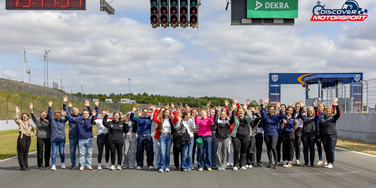 Teilnehmerinnen und Rednerinnen posieren gemeinsam für ein Gruppenfoto auf der Rennstrecke mit erhobenen Händen.