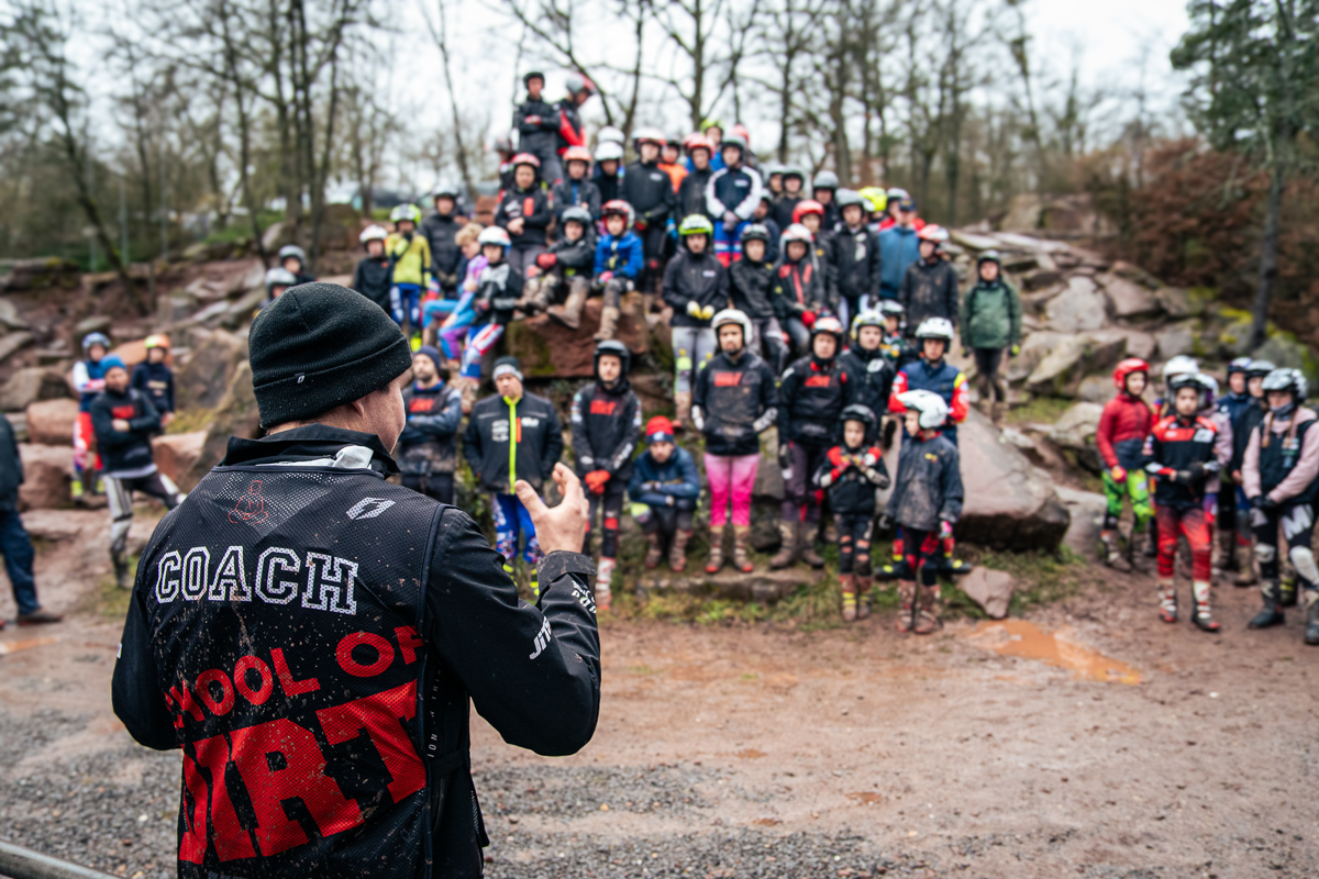 Trainer vor großer Gruppe Trialfahrern im Hintergrund