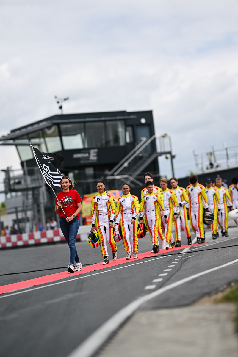 Teilnehmer der FIA Academy Trophy Senior gehen in Mülsen zur Fahrerparade an der Start-/Zielgeraden.
