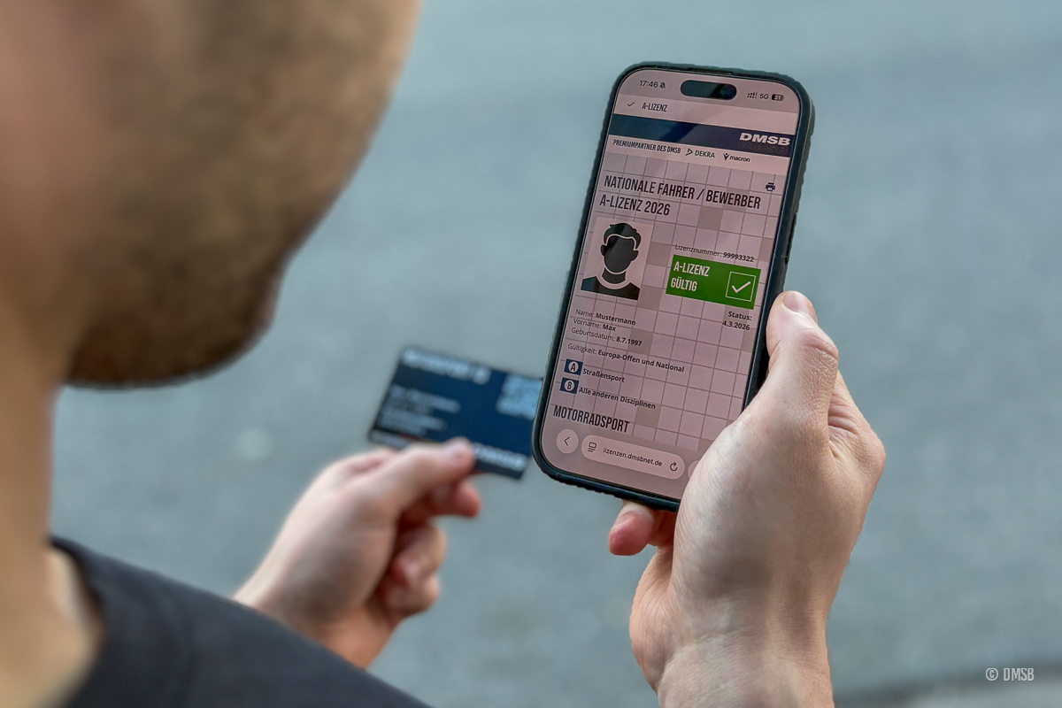 Eine Person hält ein Smartphone in der Hand, auf dem eine digitale gültige DMSB A-Lizenz 2026 zu sehen ist und hat im Hintergrund in der anderen Hand die Motorsport-ID-Checkkarte